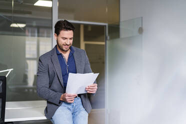 Lächelnder Geschäftsmann, der ein Dokument im Büro analysiert - DIGF17494