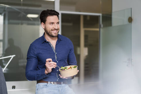 Lächelnder Geschäftsmann mit Salatschüssel in der Pause im Büro - DIGF17498