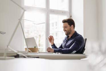 Smiling businessman on video call through laptop at office - DIGF17506