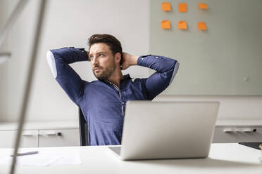 Geschäftsmann mit Händen hinter dem Kopf am Laptop am Arbeitsplatz - DIGF17509