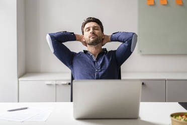 Businessman relaxing with hands behind head at office - DIGF17510