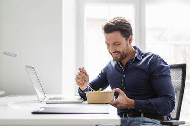 Lächelnder Geschäftsmann mit Salat am Schreibtisch im Büro - DIGF17511