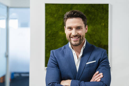 Smiling businessman with arms crossed at office - DIGF17516