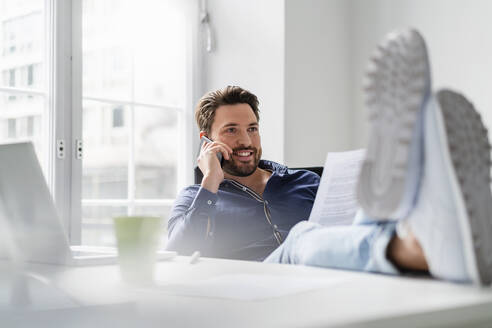 Geschäftsmann mit Dokument im Gespräch über Smartphone im Büro - DIGF17521