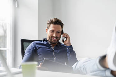 Lächelnder Geschäftsmann mit Tablet-PC im Gespräch über Smartphone im Büro - DIGF17523