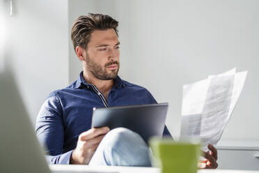 Geschäftsmann mit Tablet-PC, der ein Dokument im Büro analysiert - DIGF17529