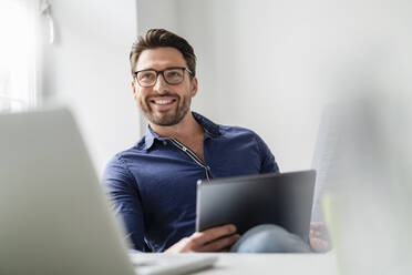 Lächelnder Geschäftsmann mit Tablet-PC und Brille im Büro - DIGF17531