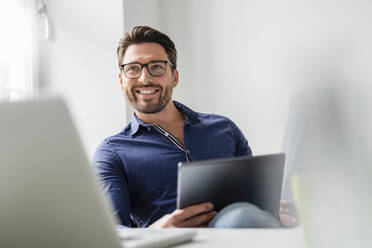 Smiling businessman with tablet PC wearing eyeglasses in office - DIGF17531