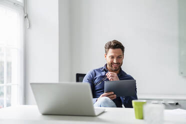 Geschäftsmann arbeitet an einem Tablet-PC mit Laptop am Schreibtisch im Büro - DIGF17532