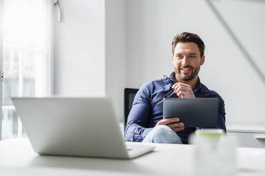 Geschäftsmann mit Laptop und Tablet-PC am Schreibtisch im Büro - DIGF17533