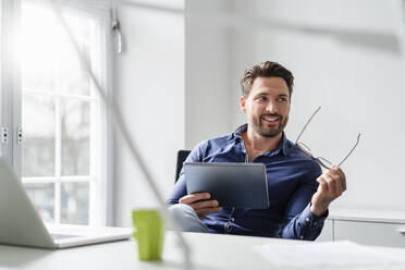 Nachdenklicher Geschäftsmann mit Brille und Tablet-PC im Büro - DIGF17534