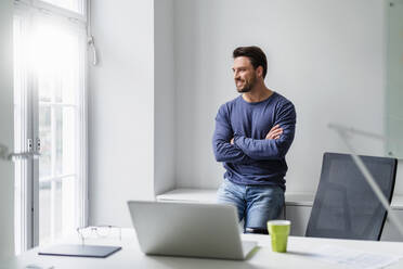 Smiling businessman looking through window at office - DIGF17542