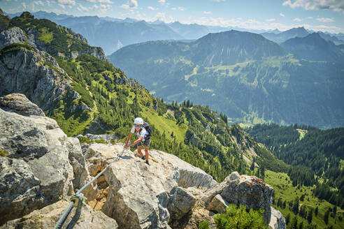 Boy climbing rock on sunny day - DIKF00600