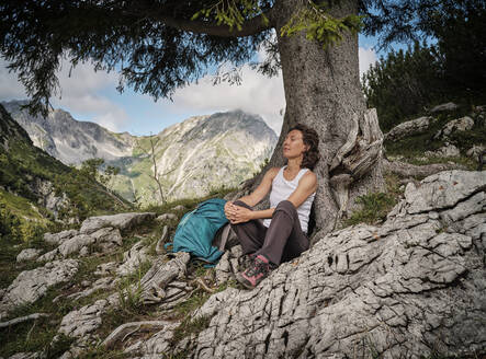 Woman with eyes closed resting by tree - DIKF00603