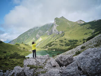 Woman standing on rock photographing mountains - DIKF00607