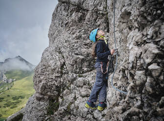 Mädchen mit Helm schaut auf einen felsigen Berg - DIKF00610