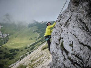 Frau mit Helm klettert auf felsigen Berg - DIKF00612
