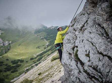 Woman wearing helmet climbing rocky mountain - DIKF00612