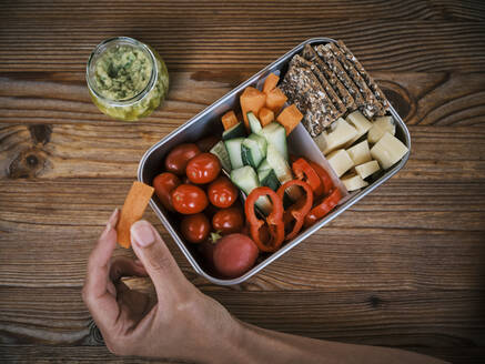 Woman with box of fresh salad on wooden table - DIKF00617