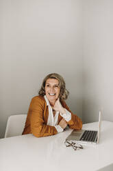 Happy senior freelancer sitting with laptop at desk - ELEF00015