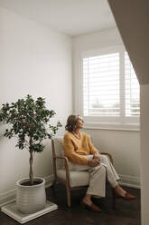 Frau sitzt auf einem Stuhl und schaut durch ein Fenster zu Hause - ELEF00022
