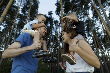 Happy parents carrying kids on shoulders enjoying in forest - TYF00072