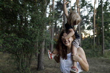Happy mother carrying daughter on shoulder in forest - TYF00073