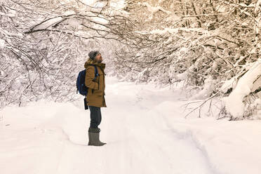 Männlicher Wanderer steht mitten auf einem verschneiten Waldweg - KNTF06607