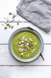 Studio shot of bowl of vegan pea soup with zucchini, broccoli, pistachios and coconut shreds - SARF04673