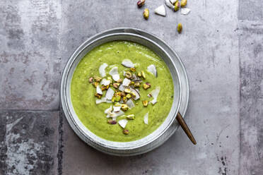 Studio shot of bowl of vegan pea soup with zucchini, broccoli, pistachios and coconut shreds - SARF04674