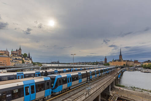 Schweden, Stockholm County, Stockholm, Sonne scheint über U-Bahn-Züge, die Sodra Jarnvagsbron-Brücke bei bewölktem Wetter passieren - FOF12856