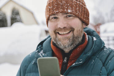 Happy man with mobile phone in winter - KNTF06621