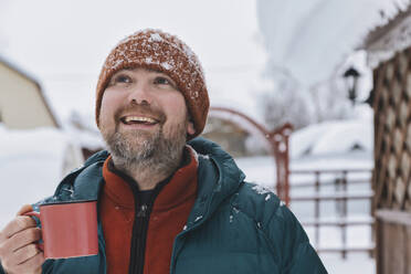 Glücklicher Mann hält Kaffeetasse und schaut im Winter nach oben - KNTF06623