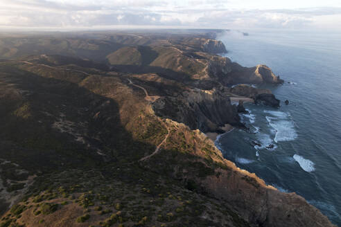 Portugal, Algarve, Vila do Bispo, Aerial view of coastal hills surrounding Castelejo Beach at dawn - MKLF00038