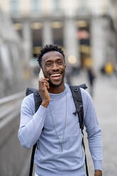 Happy young man wearing backpack talking on mobile phone - OCMF02326