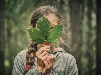 Mädchen bedeckt Gesicht mit grünem Ahornblatt - DIKF00621