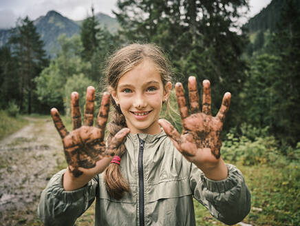 Smiling girl showing muddy hands in forest - DIKF00622