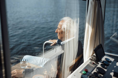 Senior man sitting at houseboat seen through windshield - GUSF06857