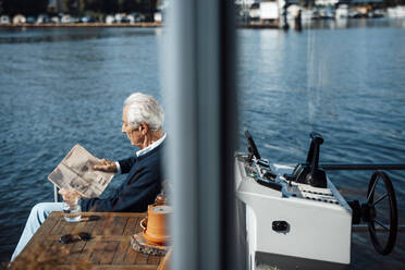 Älterer Mann liest Zeitung auf einem Hausboot an einem sonnigen Tag - GUSF06858