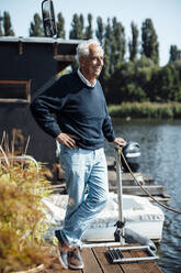 Glücklicher älterer Mann mit Hand auf der Hüfte auf einem Hausboot stehend - GUSF06875