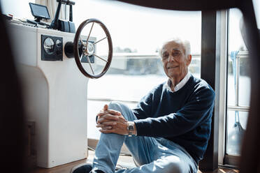 Smiling senior man sitting by window at houseboat - GUSF06879