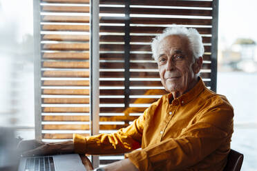 Älterer Mann sitzt mit Laptop auf einem Hausboot - GUSF06884