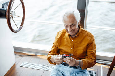 Glücklicher älterer Mann mit Drohne, der am Fenster eines Hausbootes sitzt - GUSF06888