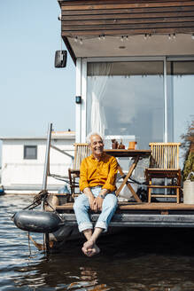 Fröhlicher älterer Mann sitzt auf einem Hausboot und genießt den sonnigen Tag - GUSF06895