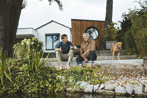 Man taking with father sitting on steps at backyard - GUSF06927