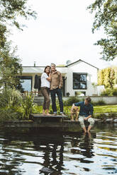 Mann mit Frau neben Sohn und Hund am See sitzend im Hinterhof - GUSF06938