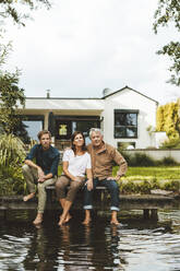 Älterer Mann mit Frau und Sohn sitzt auf Steg am See im Hinterhof - GUSF06940