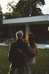 Couple with arms around standing at backyard on sunset - GUSF06965