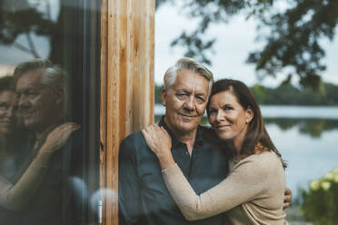 Smiling couple standing by glass wall - GUSF06972