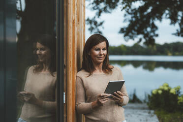 Frau mit braunen Haaren benutzt Tablet-PC an einer Glaswand im Hinterhof - GUSF06981